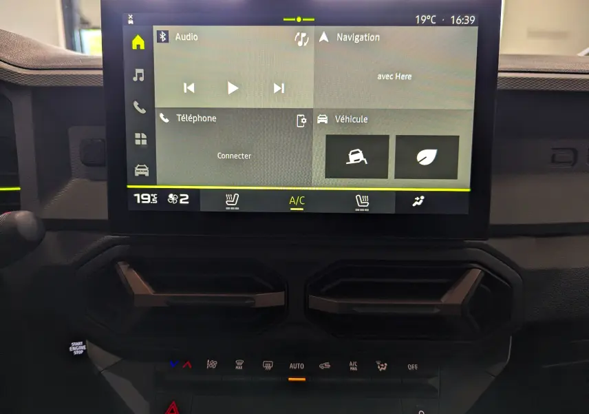 Écran tactile central du tableau de bord du Dacia Duster 2025, affichant audio, navigation et climatisation.
