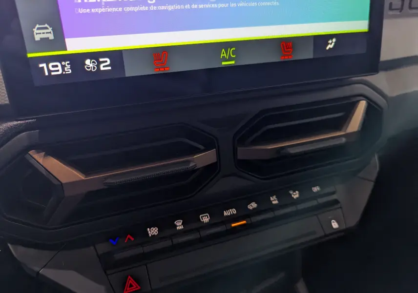 Gros plan sur la console centrale du Dacia Duster 2025 gris schiste, montrant les aérateurs hexagonaux et les commandes climatisation.