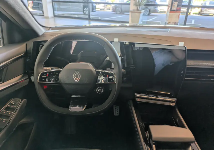 Intérieur du Renault Espace VI hybride 2025 vu de face, volant multifonction et grand écran tactile central noir.