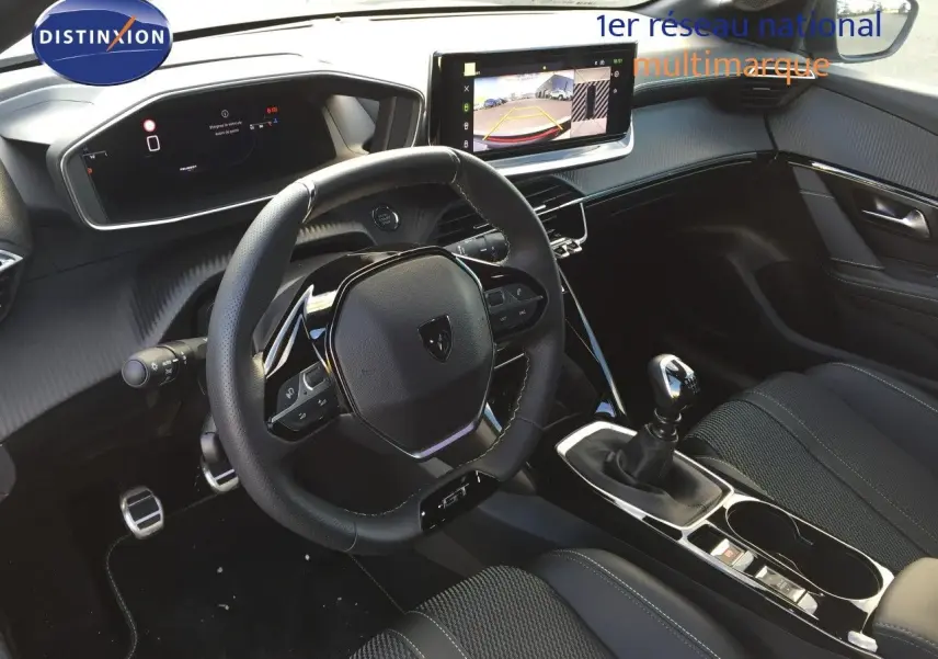 Intérieur de la Peugeot 208 2025, vue du poste de conduite avec volant GT, écran tactile et levier de vitesse manuel.