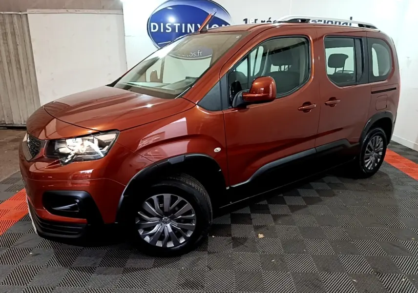 Peugeot Rifter BlueHDi 100 marron en 3/4 avant droit, avec barres de toit chromées et protections noires sur les bas de caisse.