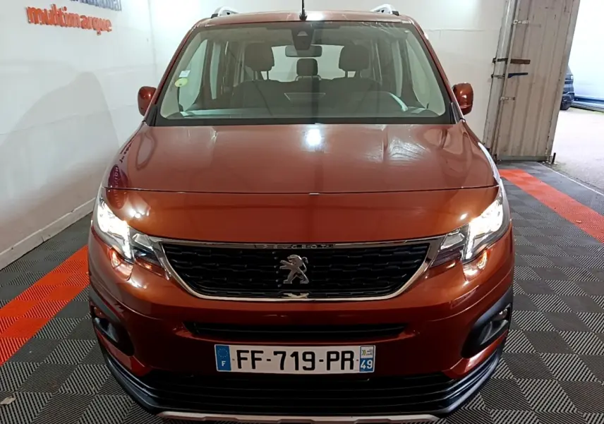 Vue avant d'un Peugeot Rifter BlueHDi 100 Allure marron avec phares allumés et calandre noire chromée.