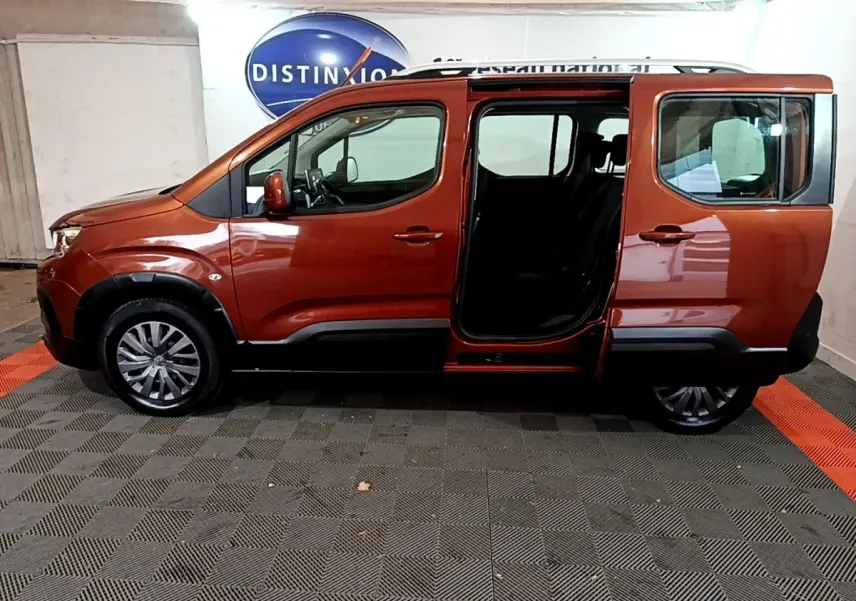 Profil côté gauche d'un Peugeot Rifter marron 2019 avec porte coulissante arrière ouverte en intérieur showroom.