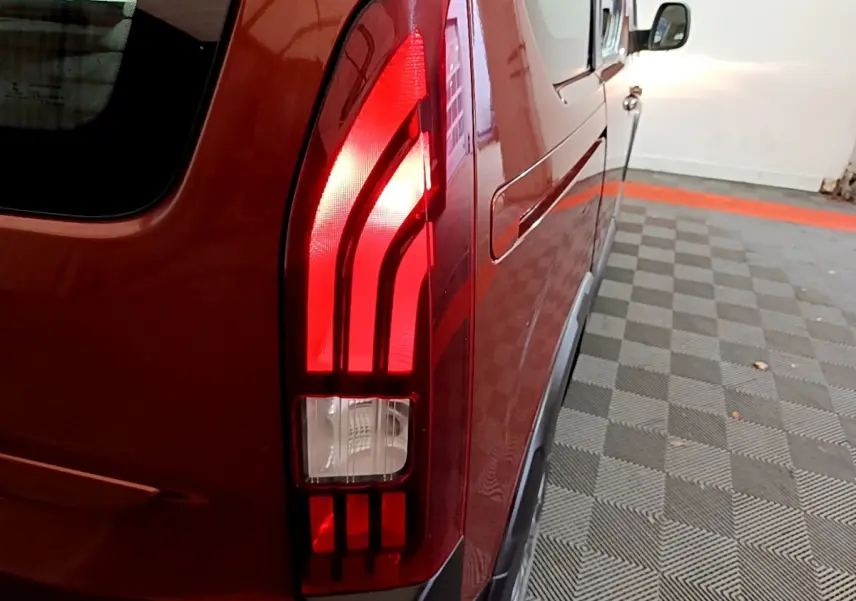 Gros plan sur le feu arrière droit rouge du Peugeot Rifter marron, avec reflet sur la carrosserie dans un parking intérieur.