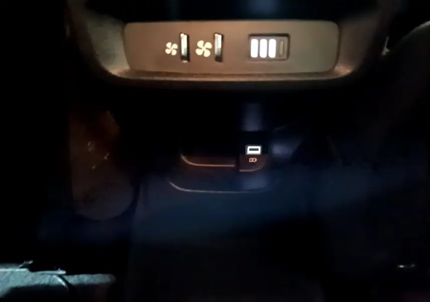 Vue rapprochée des commandes de ventilation arrière et prise USB dans l'habitacle sombre d'un Peugeot Rifter marron 2019 BlueHDi Allure.