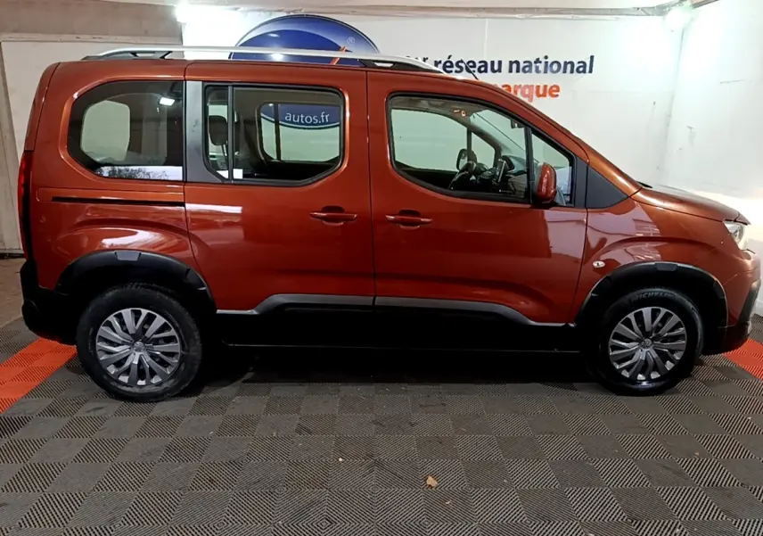 Profil droit d'un Peugeot Rifter marron 2019 avec barres de toit chromées et protections noires sur les passages de roues.