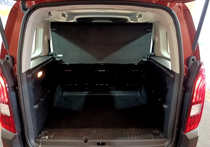 Coffre ouvert vu de l'arrière d'un Peugeot Rifter marron 2019, montrant l'espace de chargement vide et les feux arrière allumés.