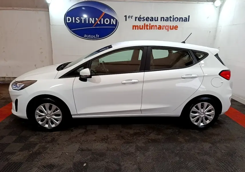 Vue de profil côté gauche d'une Ford Fiesta blanche 2022 dans un showroom avec sol noir et rouge.