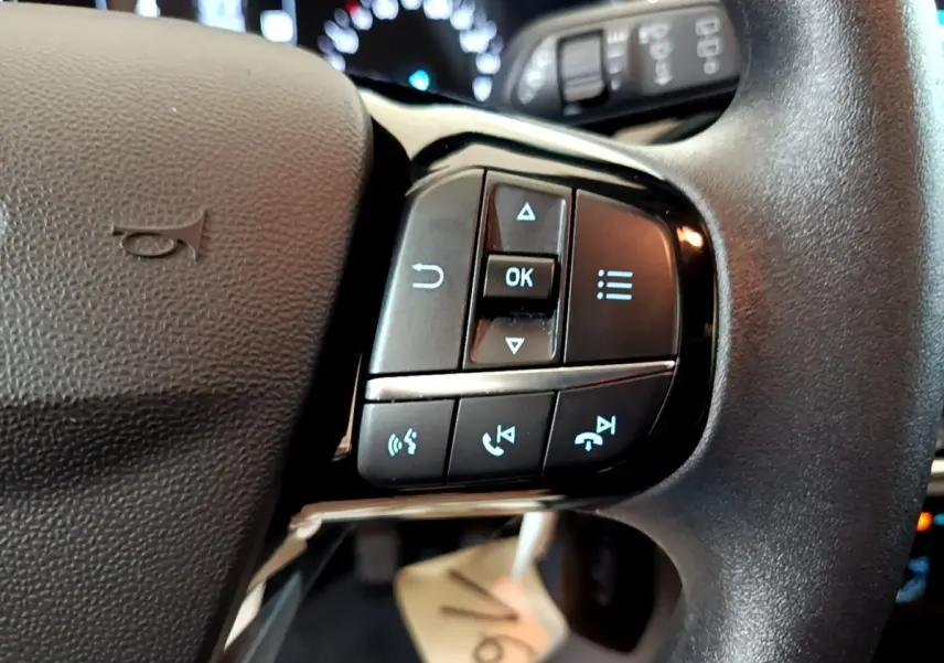Gros plan sur les commandes multifonctions au volant noir d'une Ford Fiesta blanche, avec boutons de navigation et appel.