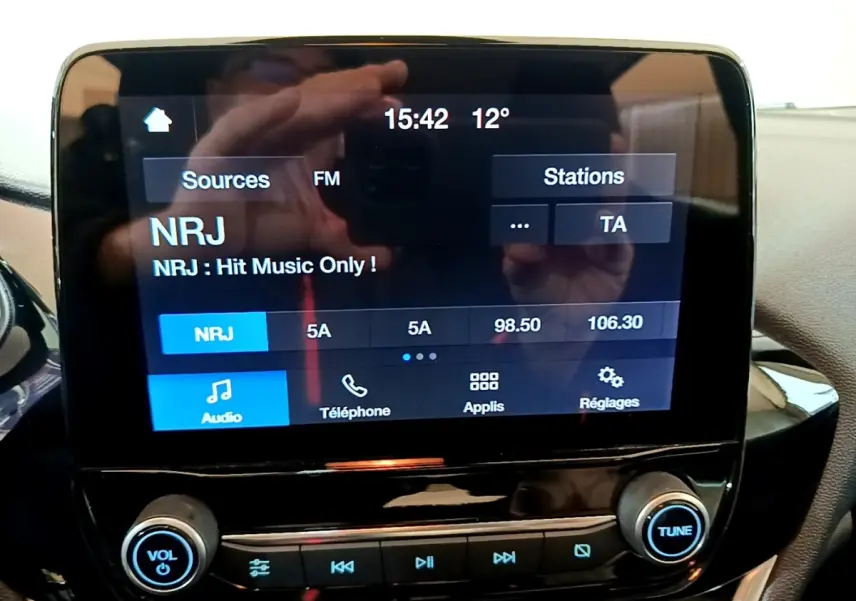 Écran tactile central de la Ford Fiesta blanche 2022 affichant la radio NRJ, vue intérieure frontale rapprochée.