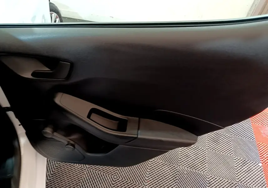 Vue intérieure sur la porte côté gauche d’une Ford Fiesta blanche, avec poignée et commande de vitre manuelle noire.