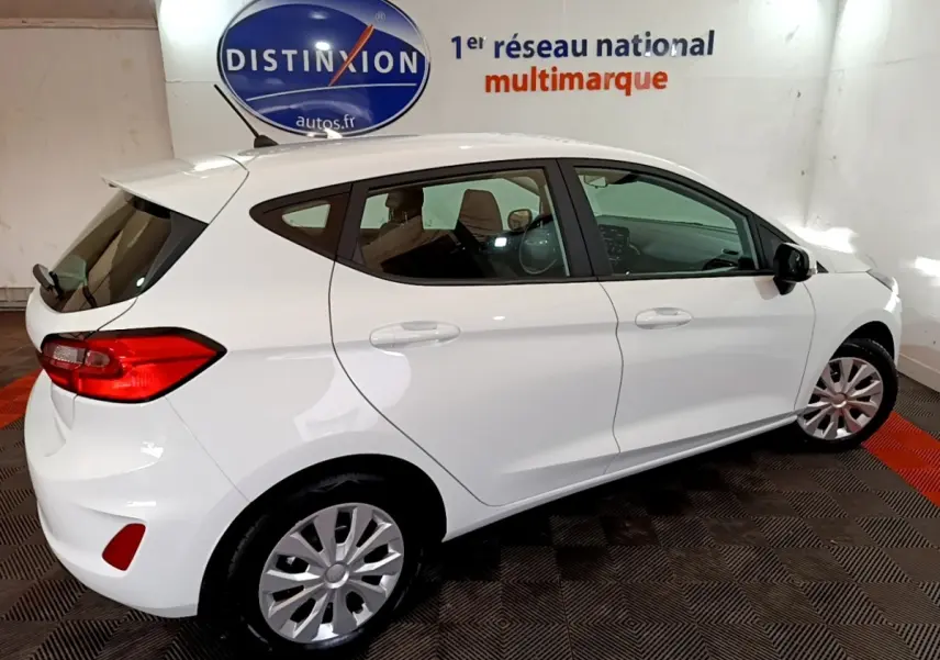 Ford Fiesta blanche vue de profil droit en intérieur, avec jantes acier et vitres teintées arrière.