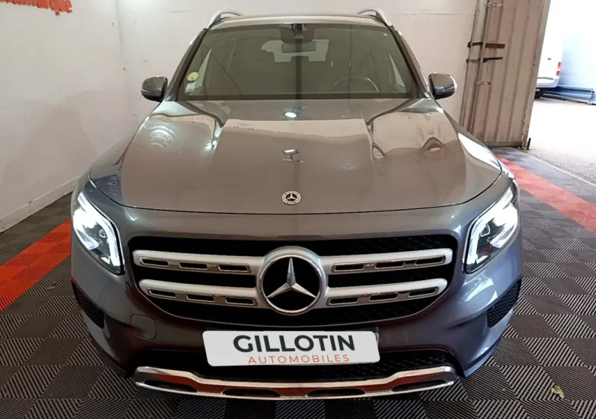 Vue avant d’un Mercedes GLB 200 d Business Line gris foncé avec calandre chromée et phares LED allumés.