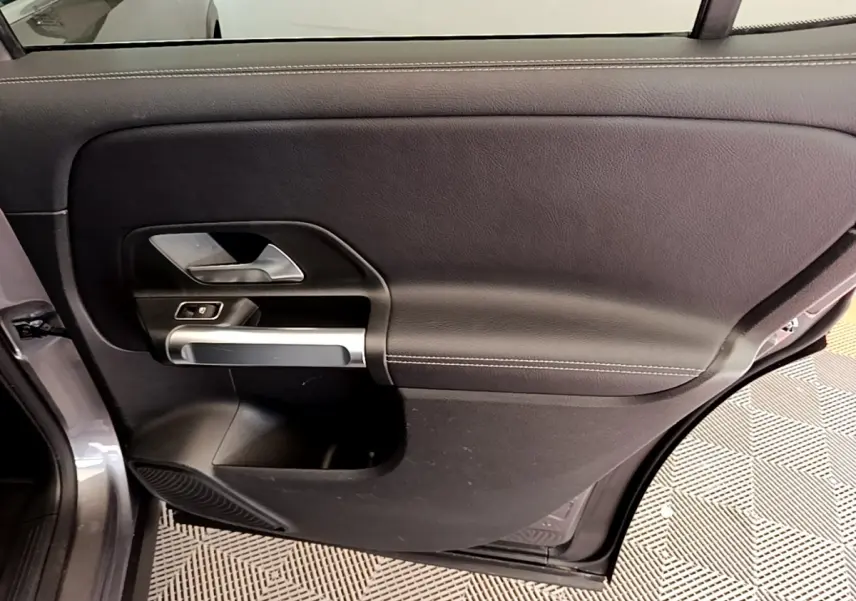 Vue intérieure de la porte arrière gauche du Mercedes GLB 200 d Business Line gris foncé, avec poignée argentée et commande de fenêtre.