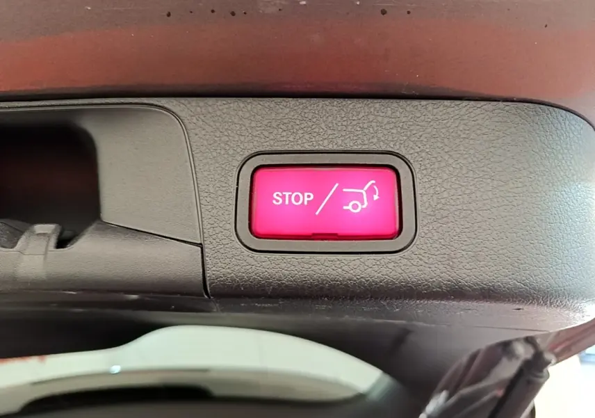 Bouton rouge STOP pour fermeture électrique du coffre, visible sur la partie intérieure du hayon d’un Mercedes GLB gris foncé.