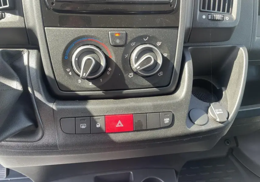 Vue rapprochée du tableau de bord noir du Citroën Jumper 2023, montrant les commandes de climatisation et les boutons de sécurité.