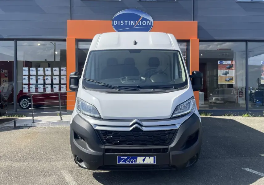 Vue frontale d’un Citroën Jumper blanc 2023 avec pare-chocs noirs, stationné devant un bâtiment commercial.
