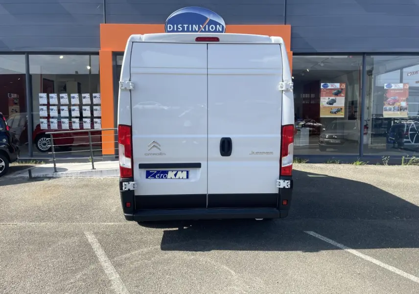 Vue arrière d’un Citroën Jumper blanc 2023 garé devant une vitrine avec portes battantes tôlées et feux rouges verticaux.