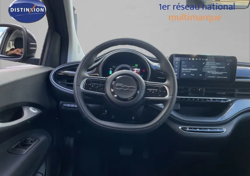 Vue intérieure frontale du tableau de bord noir onyx de la FIAT 500 électrique 2023 avec volant cuir et écran tactile.
