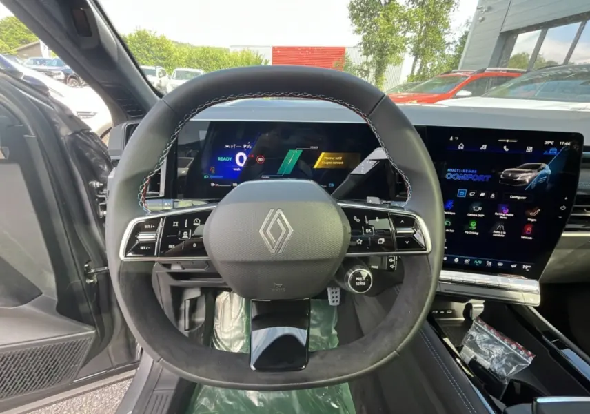 Vue intérieure centrée sur le volant cuir multifonctions du Renault Austral gris schiste avec écran digital et toit panoramique.