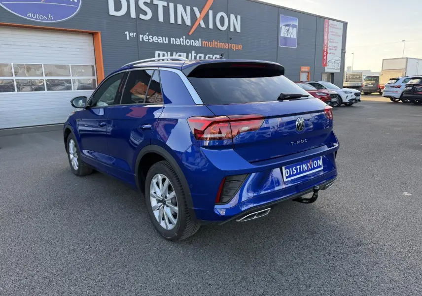 Volkswagen T-Roc bleu lapiz métallisé vu en 3/4 arrière droit avec attelage amovible et jantes alliage gris.