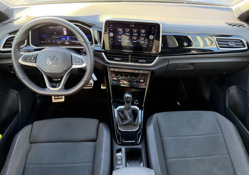 Vue intérieure frontale du tableau de bord et volant Volkswagen T-Roc 2025, finition R-Line avec écran tactile et sellerie noire.