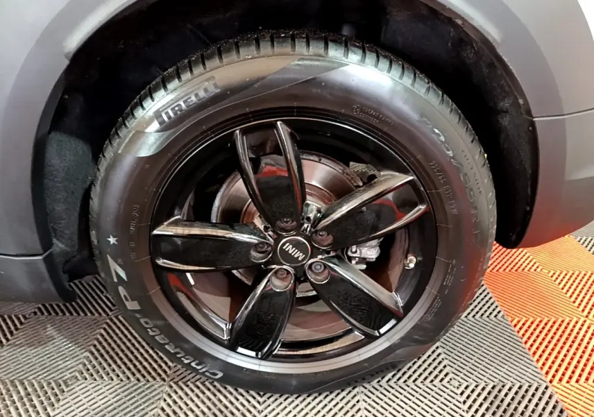 Gros plan sur la roue arrière droite d'une MINI Countryman gris clair avec jante noire brillante cinq branches.