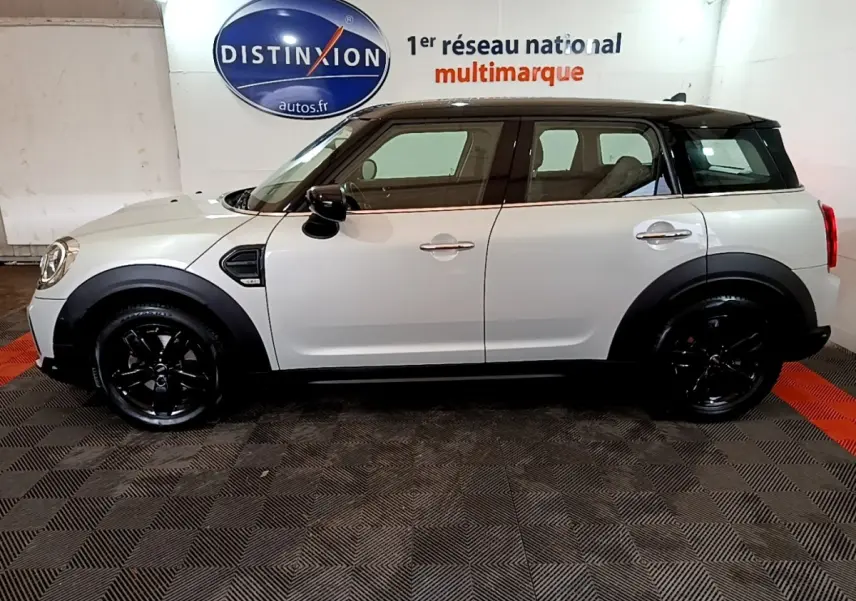 Vue de profil côté gauche d'une MINI Countryman gris clair avec toit et jantes noires dans un showroom.