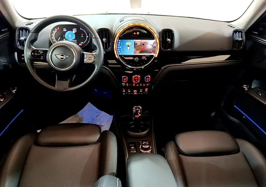 Vue intérieure avant du tableau de bord noir et volant cuir d'une MINI Countryman gris clair avec éclairage d'ambiance bleu.