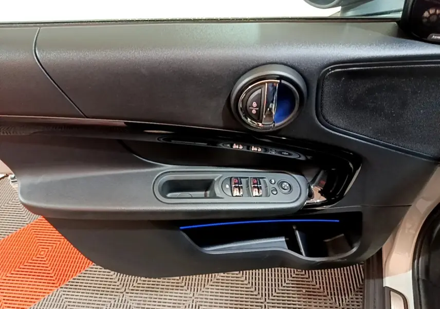 Vue rapprochée de la porte avant gauche grise d'une MINI Countryman 2022 avec éclairage d'ambiance bleu et commandes électriques.