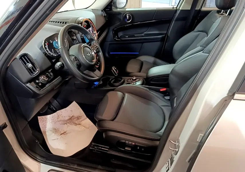 Intérieur côté conducteur du MINI Countryman gris clair 2022, sièges cuir noirs et tableau de bord avec éclairage bleu.