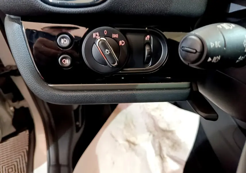 Gros plan sur les commandes d’éclairage noires à gauche du volant dans l’habitacle d’une MINI Countryman gris clair.
