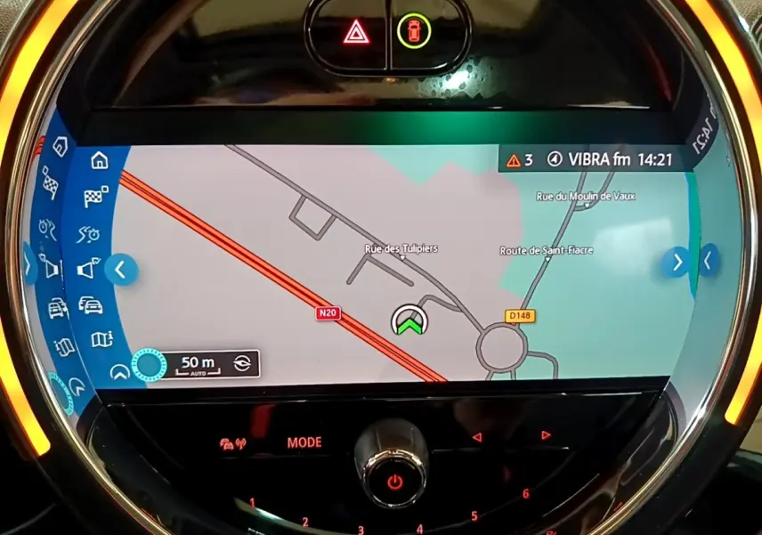 Vue rapprochée de l’écran tactile central circulaire du MINI Countryman gris clair avec navigation affichée et éclairage ambiant orange.