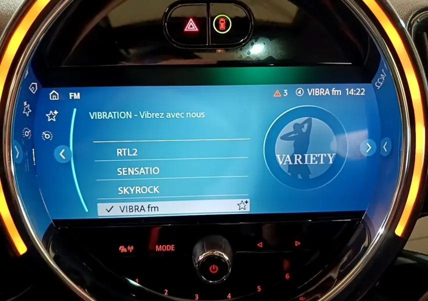 Gros plan sur l'écran tactile central rond du MINI Countryman gris clair, avec ambiance lumineuse orange autour.