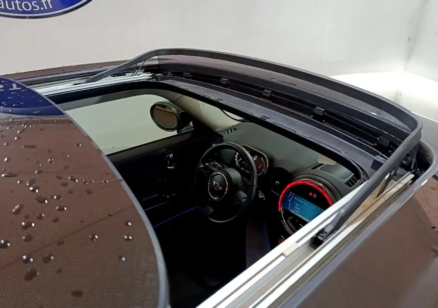 Vue plongeante sur l'intérieur d'une MINI Countryman gris clair avec toit ouvrant électrique et tableau de bord éclairé.