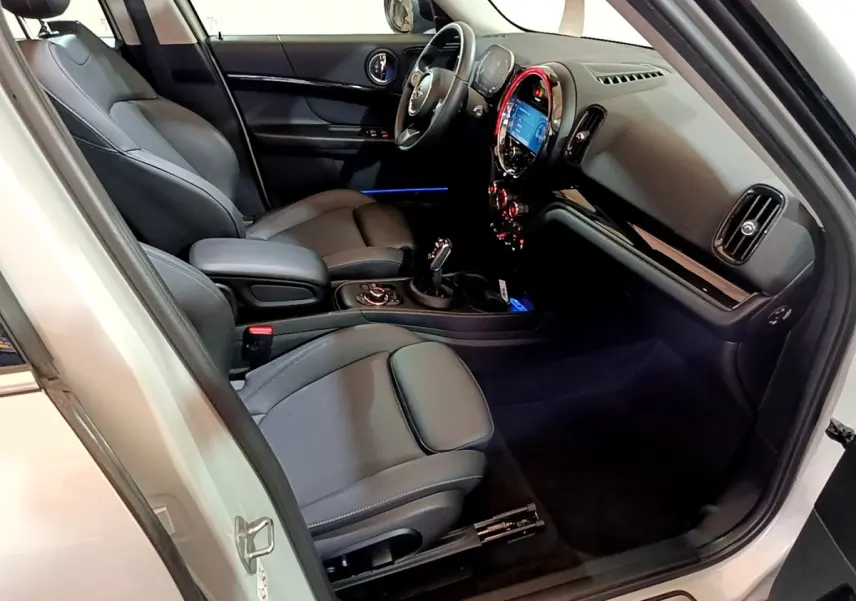 Vue intérieure côté conducteur de la MINI Countryman gris clair 2022, sièges cuir noirs et tableau de bord lumineux.