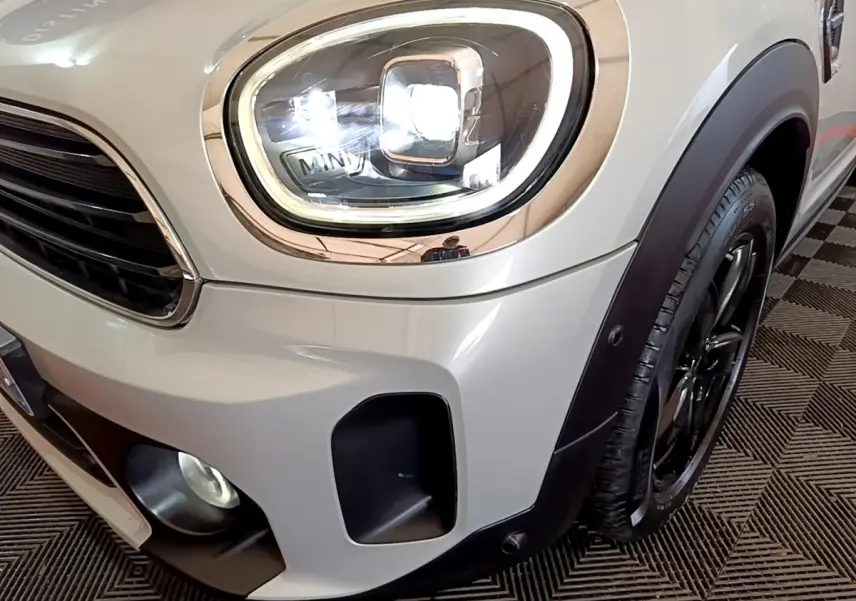 Gros plan sur le phare avant gauche et la roue d’une MINI Countryman gris clair avec détails noirs et éclairage LED.