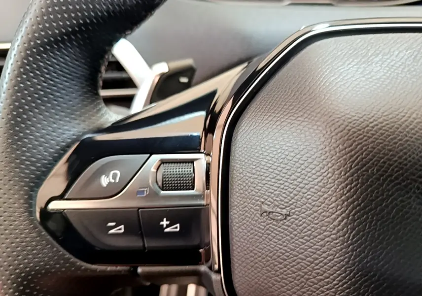 Gros plan sur le volant cuir et alu noir du Peugeot 3008 GT Pack, avec commandes multifonctions visibles à gauche.