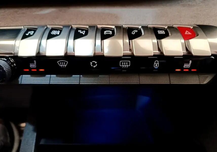 Gros plan sur la rangée de boutons argentés du tableau de bord du Peugeot 3008 noir, avec éclairage rouge des sièges chauffants.