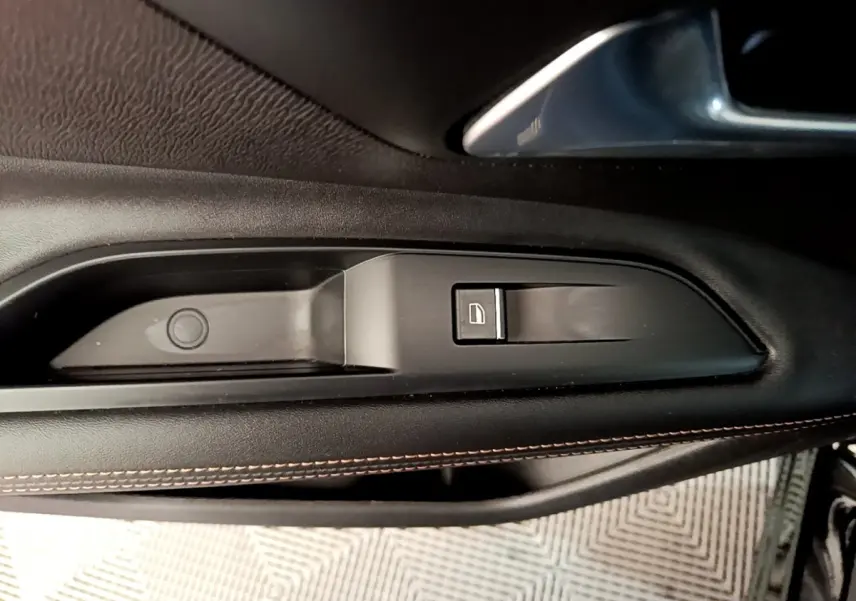 Détail de la commande de lève-vitre côté conducteur en plastique noir avec couture orange sur la porte intérieure du Peugeot 3008 noir.