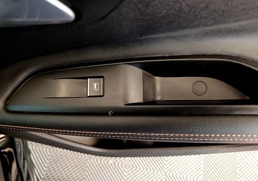Détail de la commande de lève-vitre côté gauche en plastique noir avec surpiqûres contrastantes sur la porte d’un Peugeot 3008 noir.