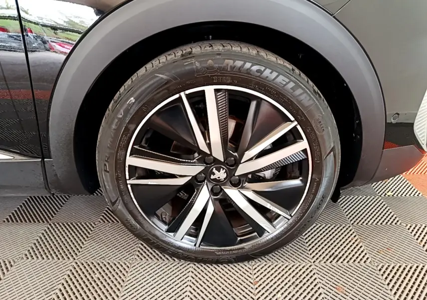 Gros plan sur la roue avant droite noire du Peugeot 3008 2022 avec jante alliage bicolore et pneu Michelin.