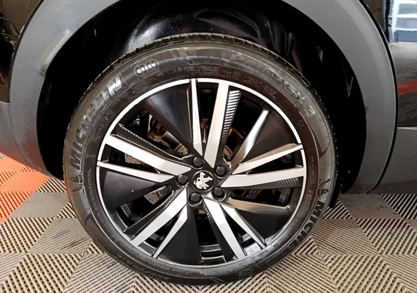 Gros plan sur la jante alliage noir et argent avec logo Peugeot, roue avant droite du 3008 noir 2022.