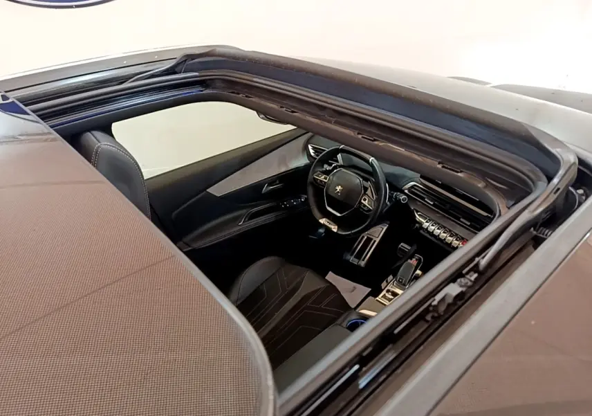 Vue intérieure par le toit ouvrant du Peugeot 3008 noir, mettant en valeur le volant cuir alu multifonctions et la console centrale moderne.