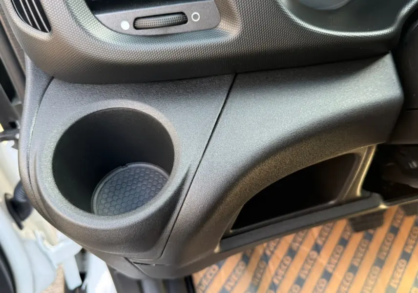 Détail intérieur montrant le porte-gobelet et le rangement côté gauche du tableau de bord d’un Iveco Daily blanc.