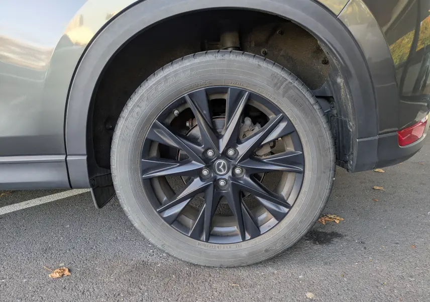 Gros plan sur la roue arrière droite grise du Mazda CX-5 2020 avec jante noire à dix branches et logo Mazda central.