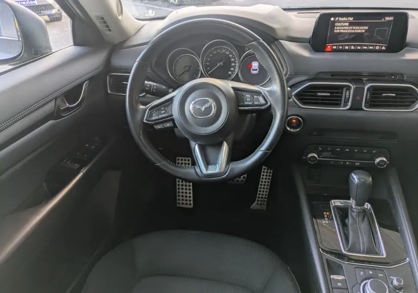 Vue intérieure du poste de conduite du Mazda CX-5 gris 2020, avec volant multifonctions et écran central tactile.