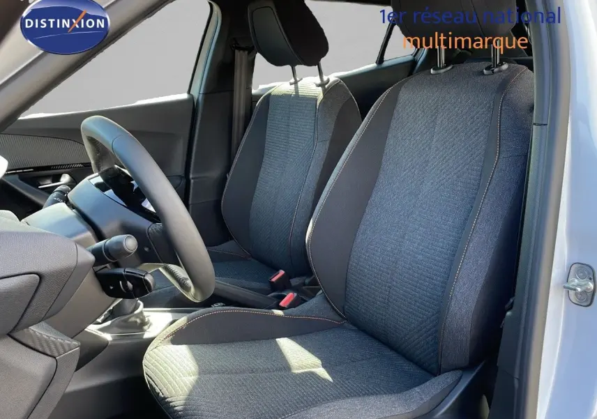 Intérieur du Peugeot 2008 blanc Okenite, vue côté conducteur montrant les sièges tissu noir et gris avec surpiqûres contrastantes.