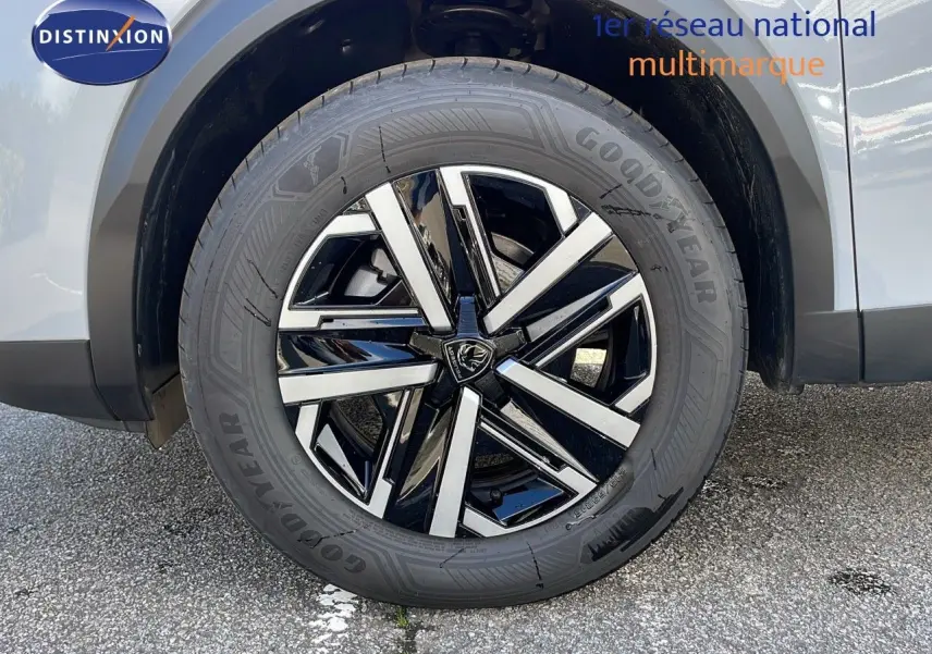 Gros plan sur la roue avant droite d'un Peugeot 2008 blanc Okenite avec jante alliage noire et argentée.