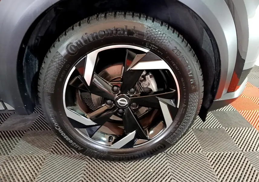 Gros plan sur la roue avant droite du Nissan Juke Hybrid 143 Business+ noir avec jante alliage noire et argentée.